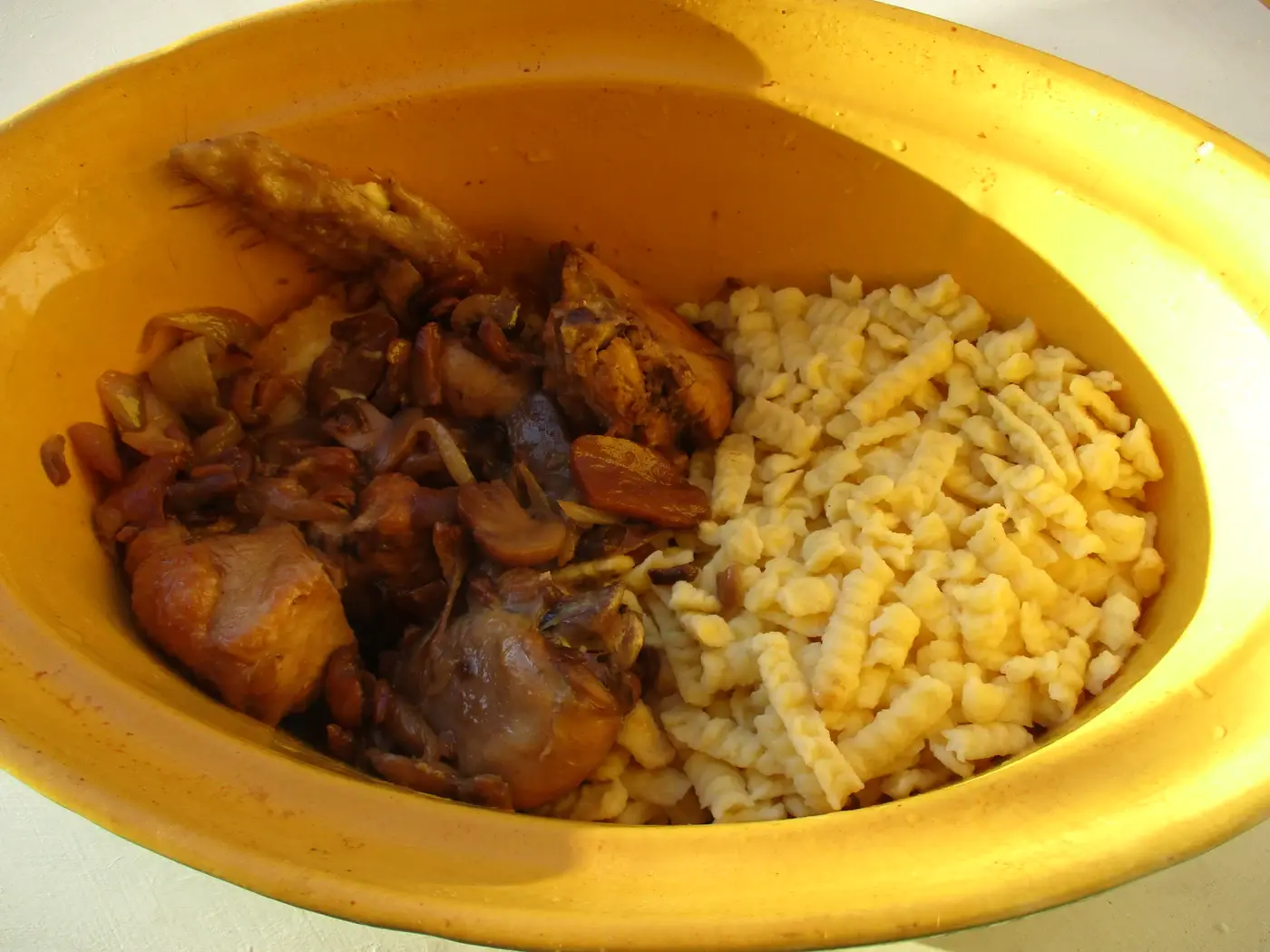 Coq au riesling servi avec des spätzle dans un plat en terre