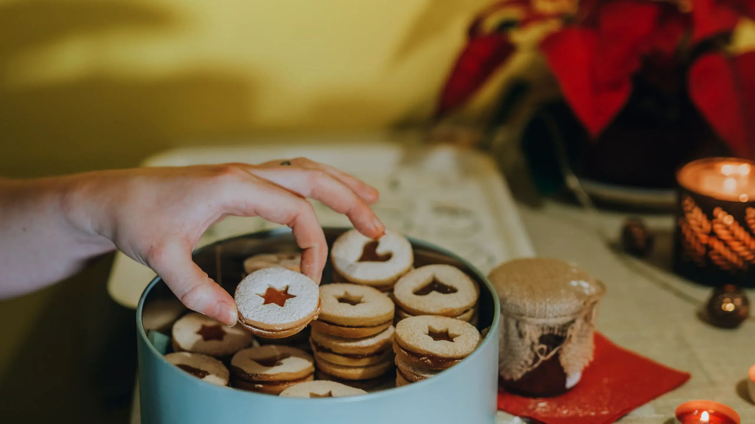 Boîte en métal remplie de petits sablés de Noël, une main en prend un