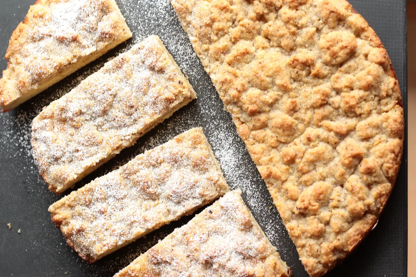 Gateau rond entierement recouvert de streusel, decoupe en parts et saupoudre de sucre glace