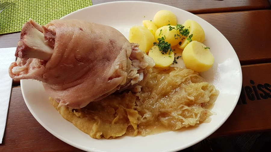 Jarret de porc poché, peau claire, servi avec de la choucroute et des pommes de terre vapeur