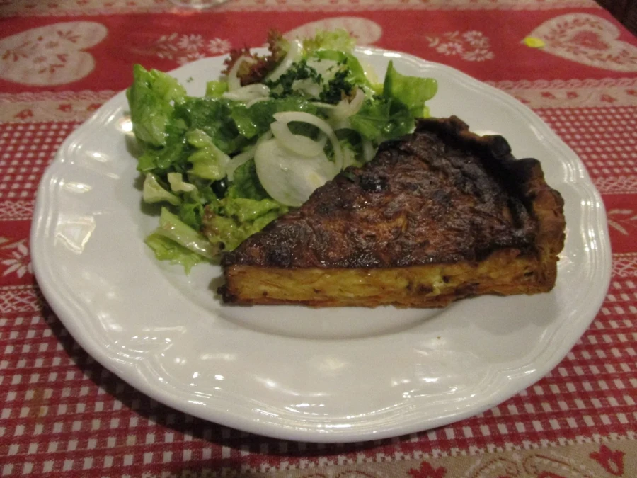 Part de tarte à l’oignon dorée servie avec une salade verte aux oignons crus