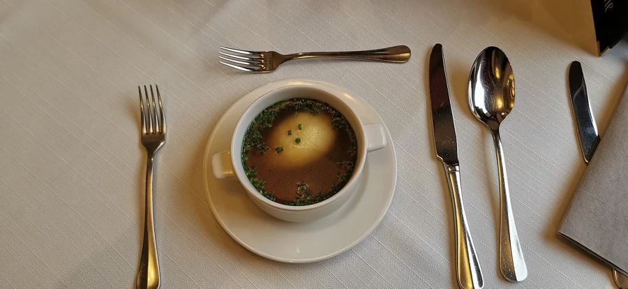Quenelle de foie dans un bouillon parsemé de ciboulette, servie dans une tasse sur une table dressée